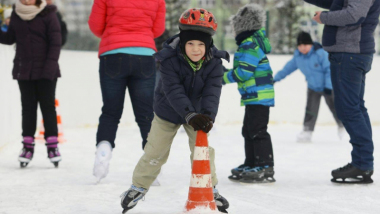 Na zdjęciu chłopiec na łyżwach na lodowisku trzyma się słupka