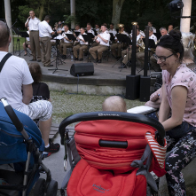 Matki z dziećmi słuchające koncertu orkiestry wojskowej w amfiteatrze na terenie parku