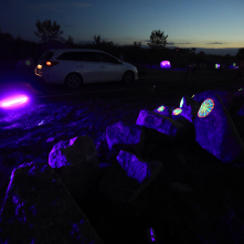 Na zdjęciu widać drobne podświetlone elementy umieszczone na kamieniach, w tle widoczny jest przejeżdżający samochód