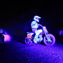 Dwóch zawodników motocrossu, oświetlonych na fioletowo, wjeżdża na teren festiwalu Auto Skyway