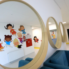 W lustrach zawieszonych na korytarzu żłobka odbijają się kolorowe postaci dziecięce naklejone na przeciwległej ścianie