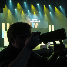 Na zdjęciu: fotograf robiący zdjęcia uczestnikom konferencji, w tle ekran z logo Firma Przyszłości