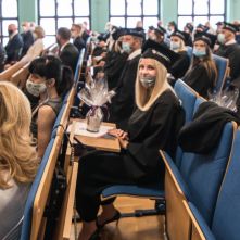 Uśmiechnięta absolwentka po odbiorze dyplomu i upominku siedzi w ławce