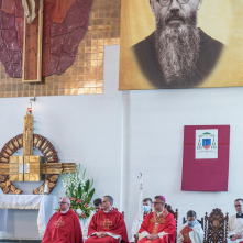 Koncelebrujący mszę księża w czerwonych szatach siedzą w prezbiterium