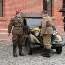 Zabytkowy pojazd i dwóch żołnierzy na tle Muzeum Twierdzy Toruń.