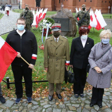 Uczestnicy uroczystości stoją z flagą biało-czerwoną przy obelisku