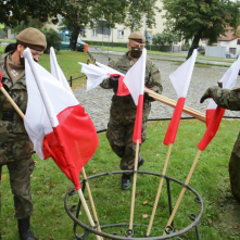 Żołnierze rozkładają flagi biało-czerwone przy obelisku
