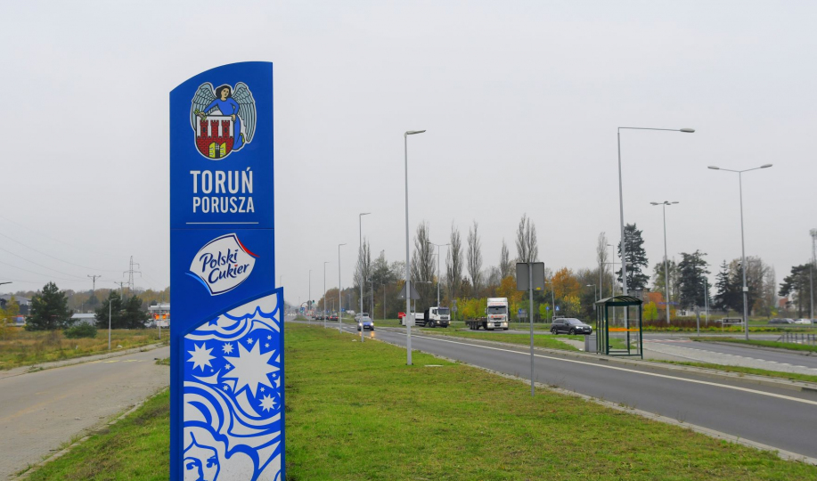 Na zdjęciu niebiesko-biały witacz przy drodze wjazdowej do Torunia