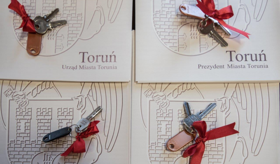 Na czterech teczkachz napisem "Toruń. urząd Miasta Torunia" leżą cztery klucze do mieszkań z przywiązaną czerwoną wstążką