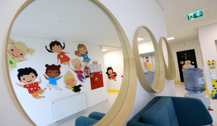 W lustrach zawieszonych na korytarzu żłobka odbijają się kolorowe postaci dziecięce naklejone na przeciwległej ścianie