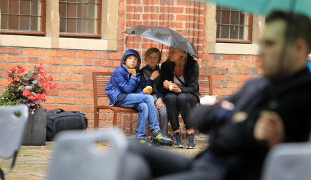 widzowie pod parasolami słuchają aktorów