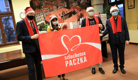 Kierownictwo Urzędu Miasta w czapkach Mikołaja trzyma flagę z logo Szlachetnej Paczki