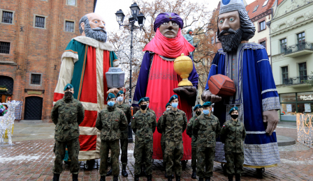 Figury trzech króli stoją na Rynku Staromiejskim, przed nimi żołnierze pozują do zdjęcia