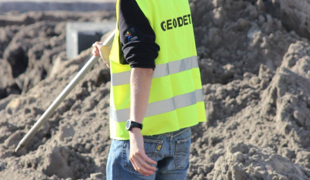 Młody mężczyzna z urządzeniem mierniczym w kamizelce z napisem Geodeta