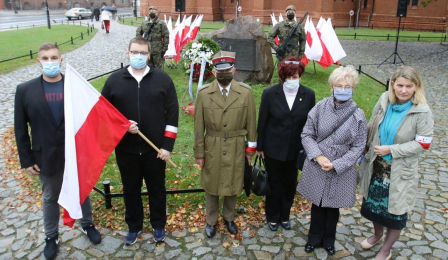 Uczestnicy uroczystości stoją z flagą biało-czerwoną przy obelisku