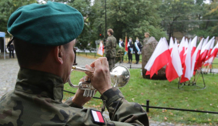 Trębacz wojskowy przy obelisku, przy którym ustawione sa flagi państwowe
