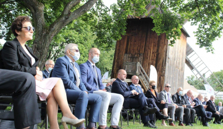 Przedstawiciele samorządów województwa kujawsko-pomorskiego siedzą na krzesłach podczas wystąpień w trakcie Forum, które odbywa się na terenie Muzeum Etnograficznego, w tle widać drewniany wiatrak